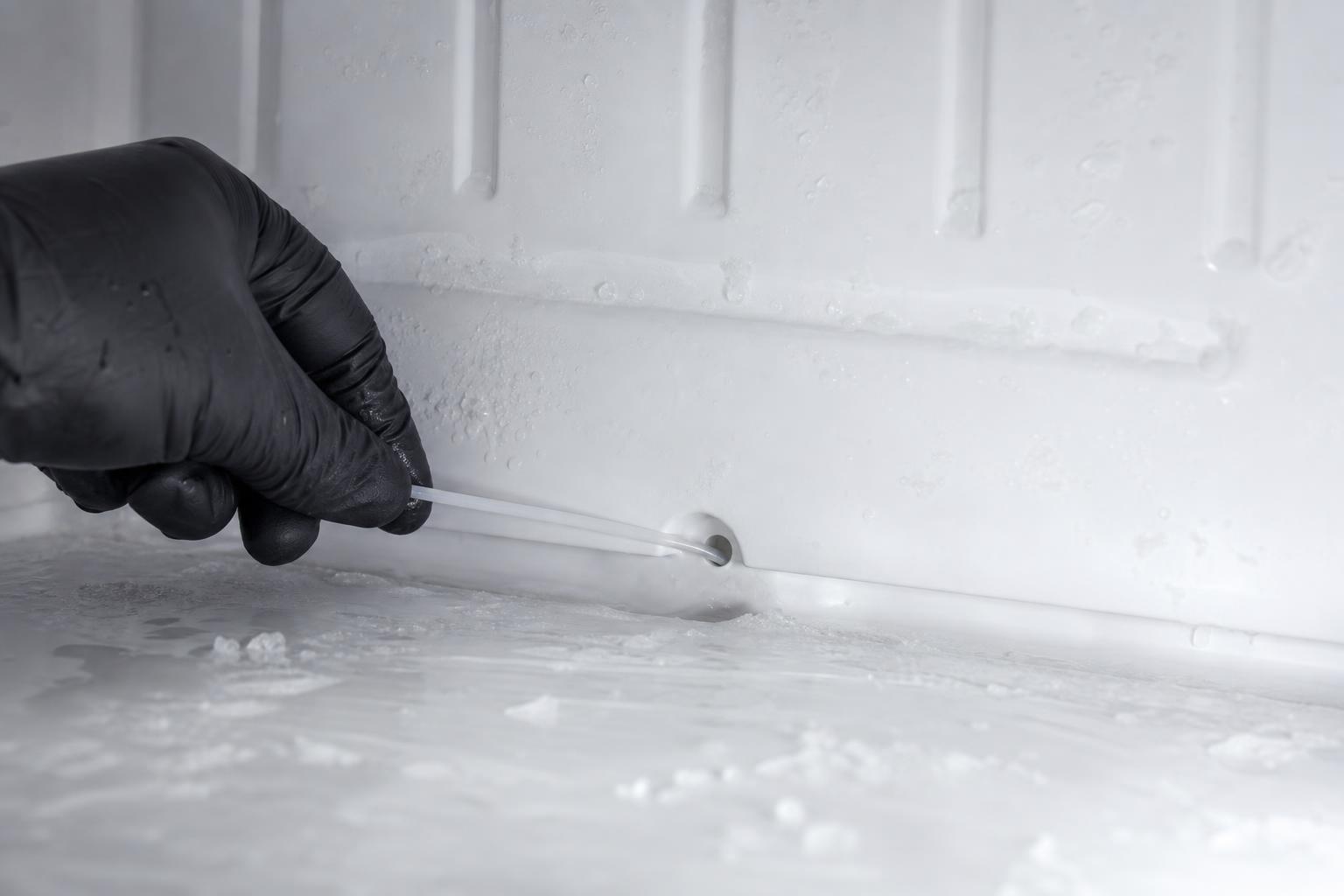 Dreno interno da geladeira sendo desobstruído com haste flexível durante a limpeza