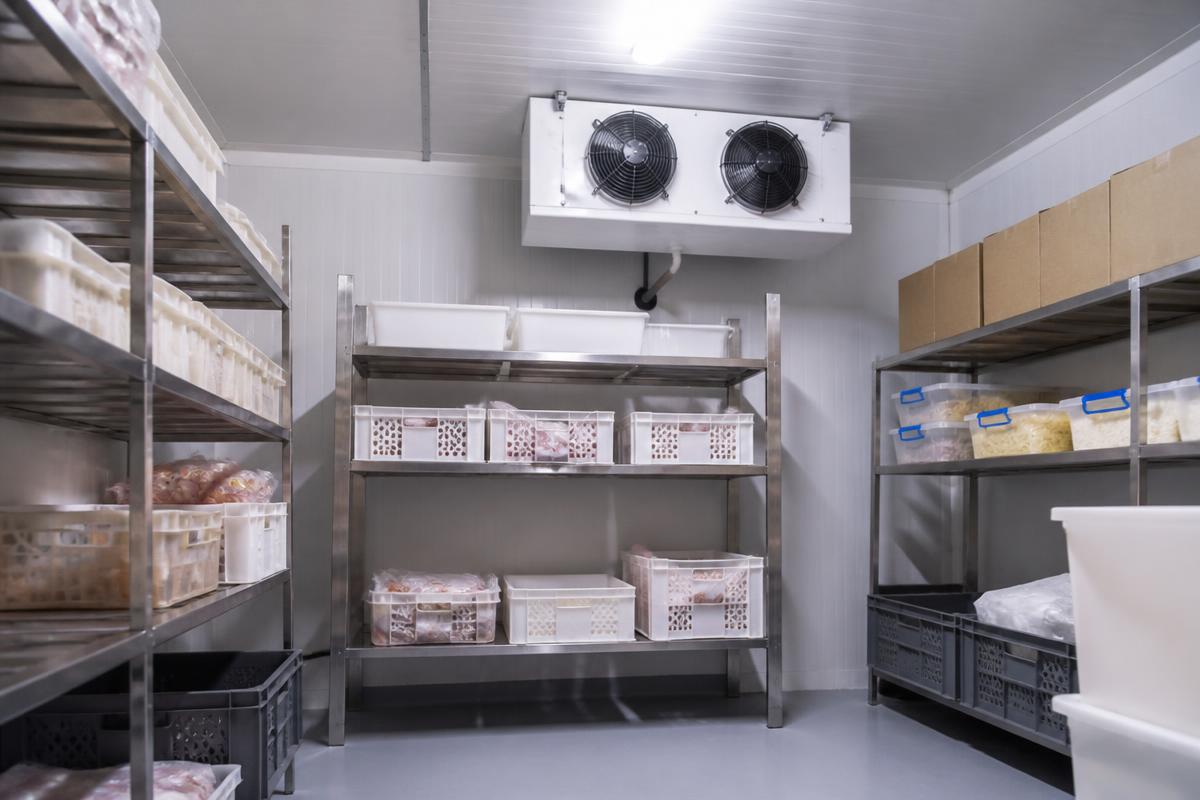 Interior de câmara fria comercial com evaporador no teto e prateleiras de inox