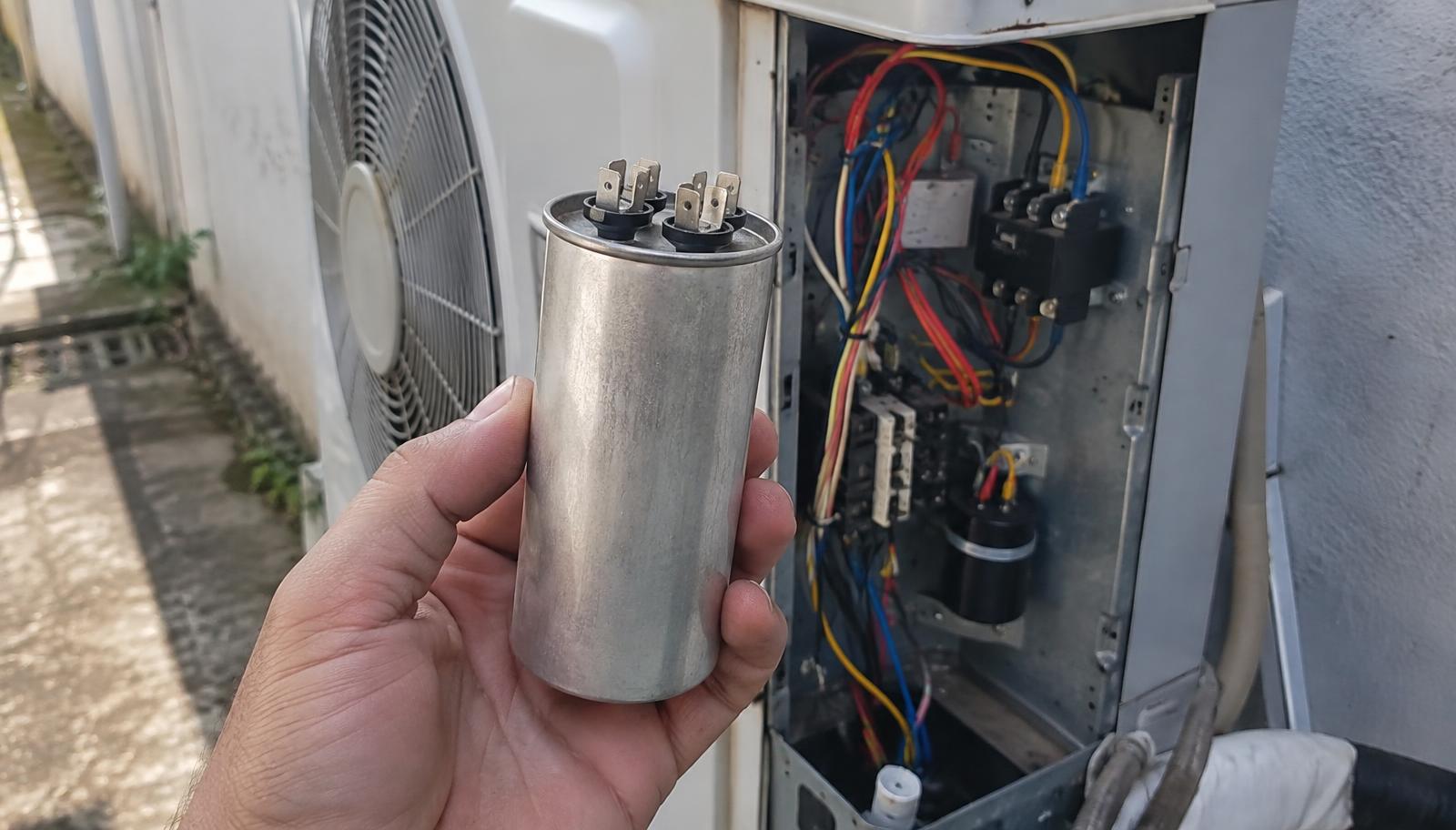 Capacitor cilíndrico de ar-condicionado segurado na frente da unidade condensadora de um split