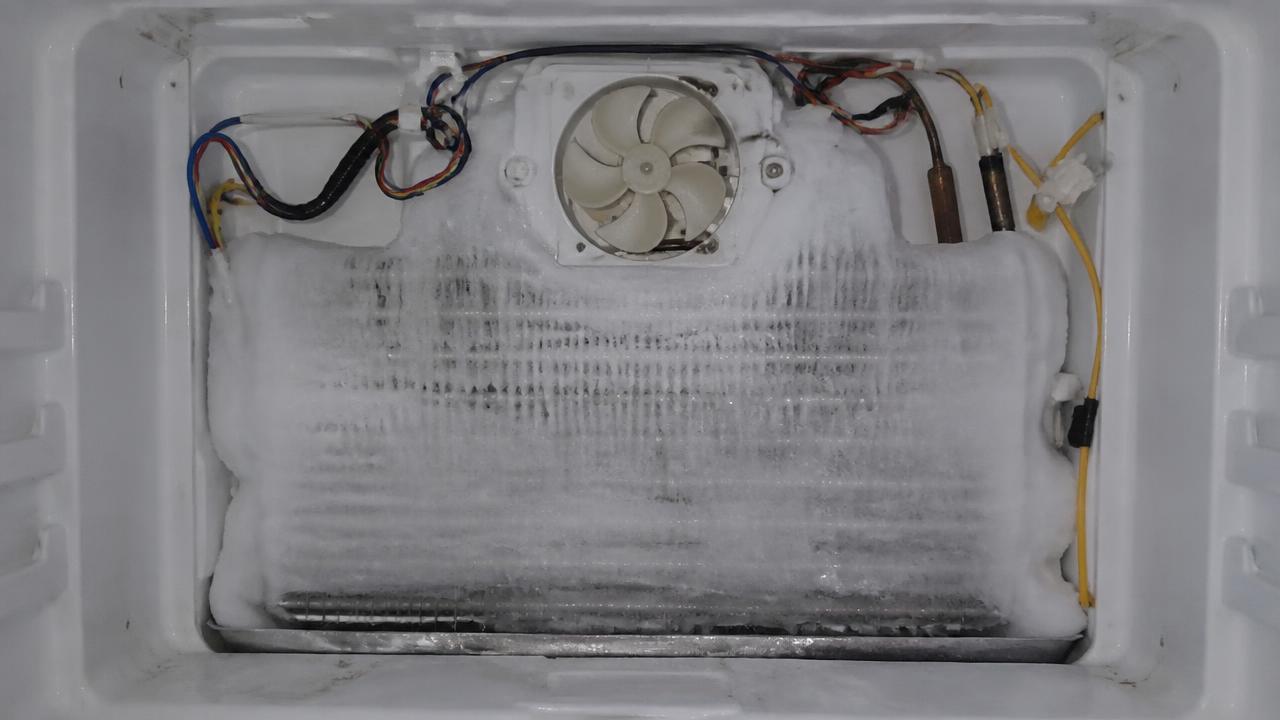 Evaporador de geladeira frost free tomado por bloco de gelo, com o ventilador travado, atrás da tampa interna do freezer