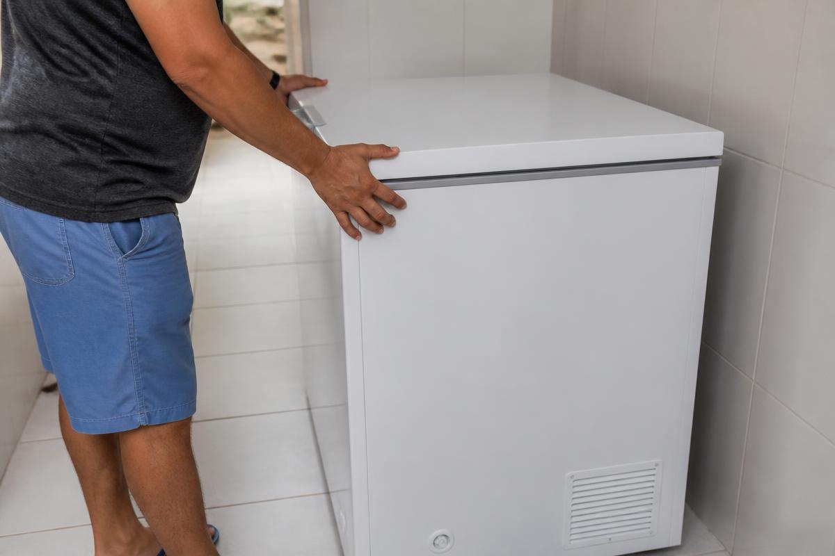Pessoa afastando o freezer da parede para eliminar vibração contra o móvel