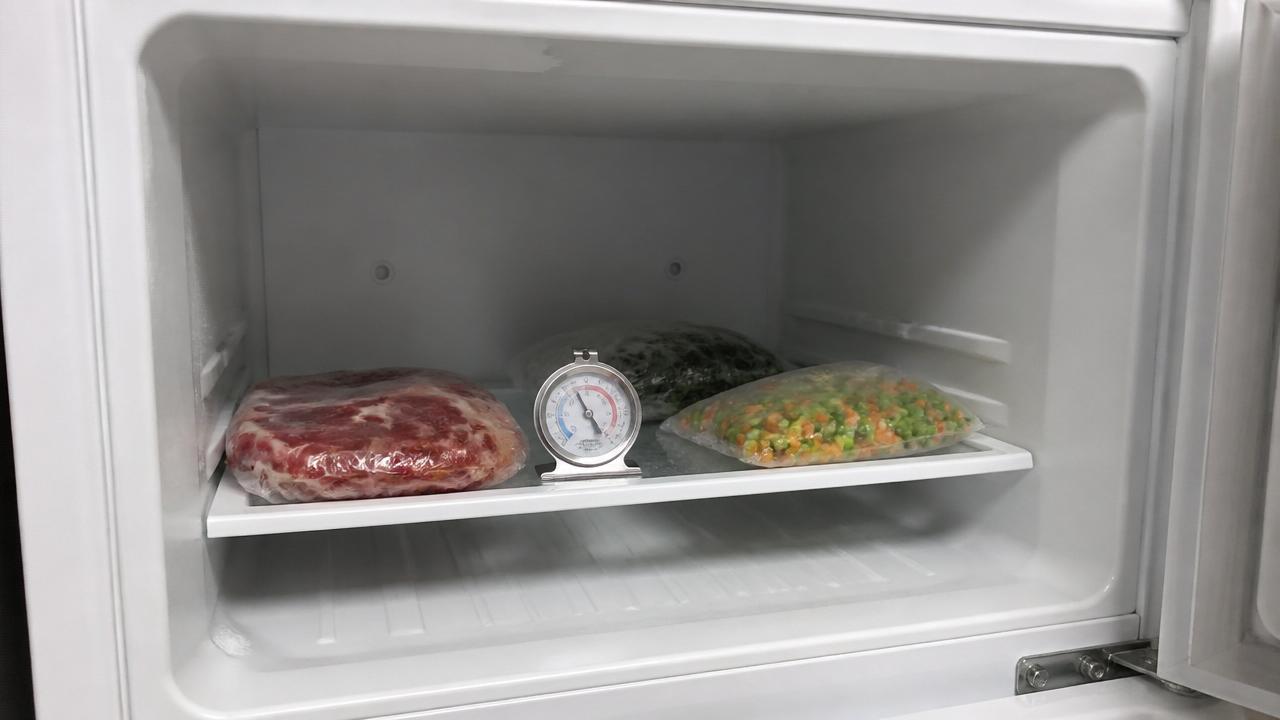 Interior de um freezer com alimentos apenas gelados, sem camada de congelamento, e um termômetro à vista