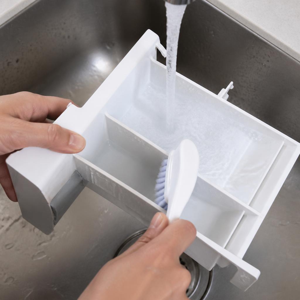 Mãos lavando a gaveta dispenser da máquina de lavar sob água corrente, escovando o resíduo com escova pequena