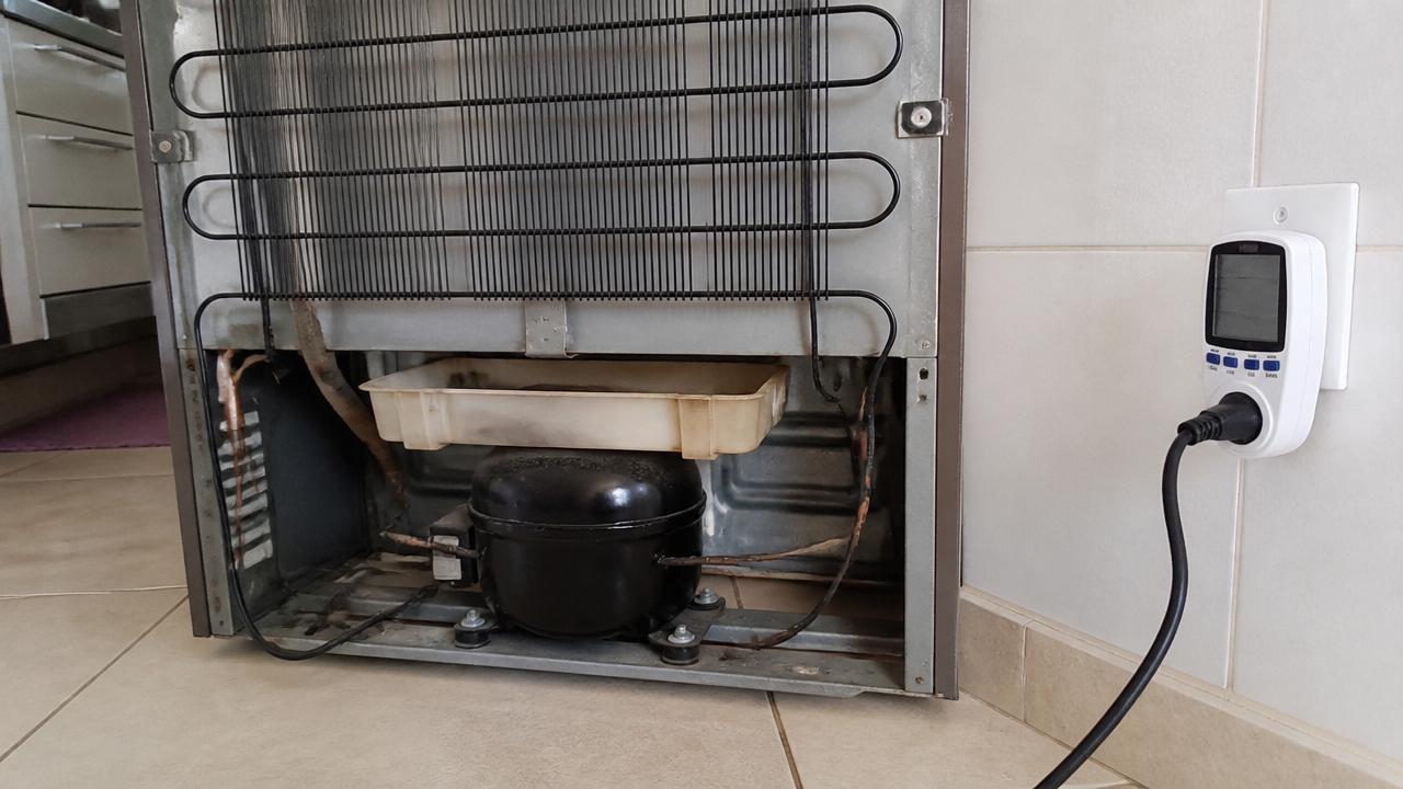 Medidor de energia ao lado de uma geladeira com o compressor visivelmente em funcionamento contínuo