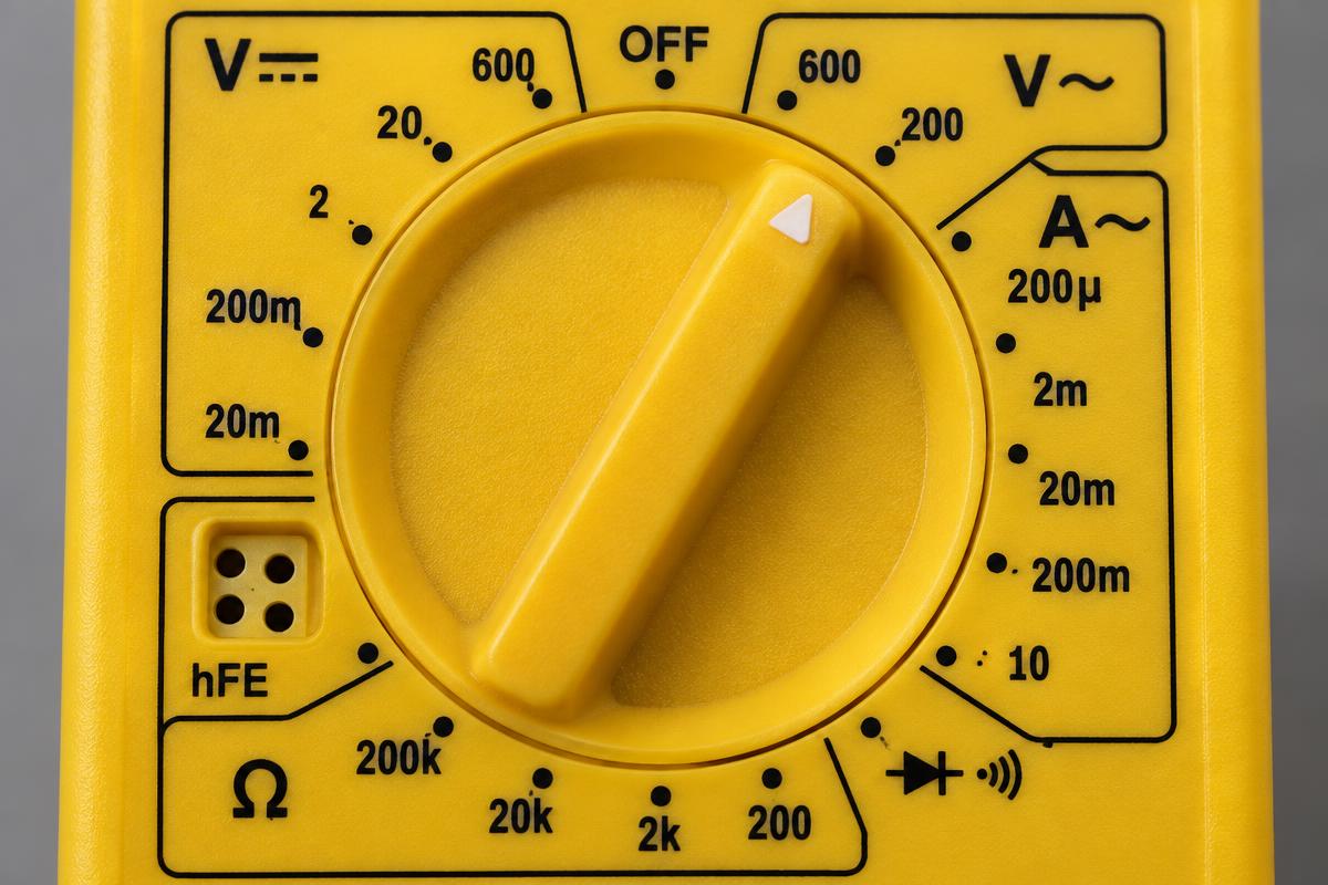 Macro do seletor de um multímetro digital de bolso amarelo com escalas numeradas de tensão, corrente e resistência