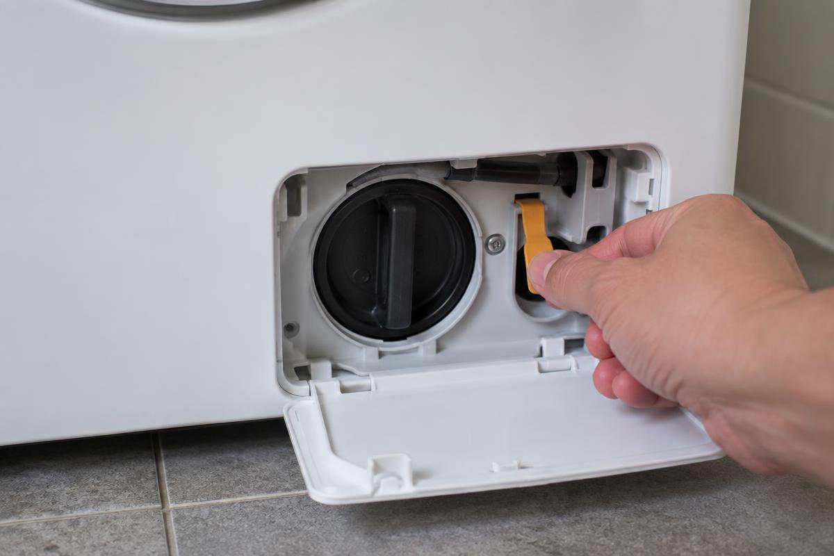 Mão puxando cabo plástico de destravamento manual de emergência dentro do painel inferior de uma lava e seca.