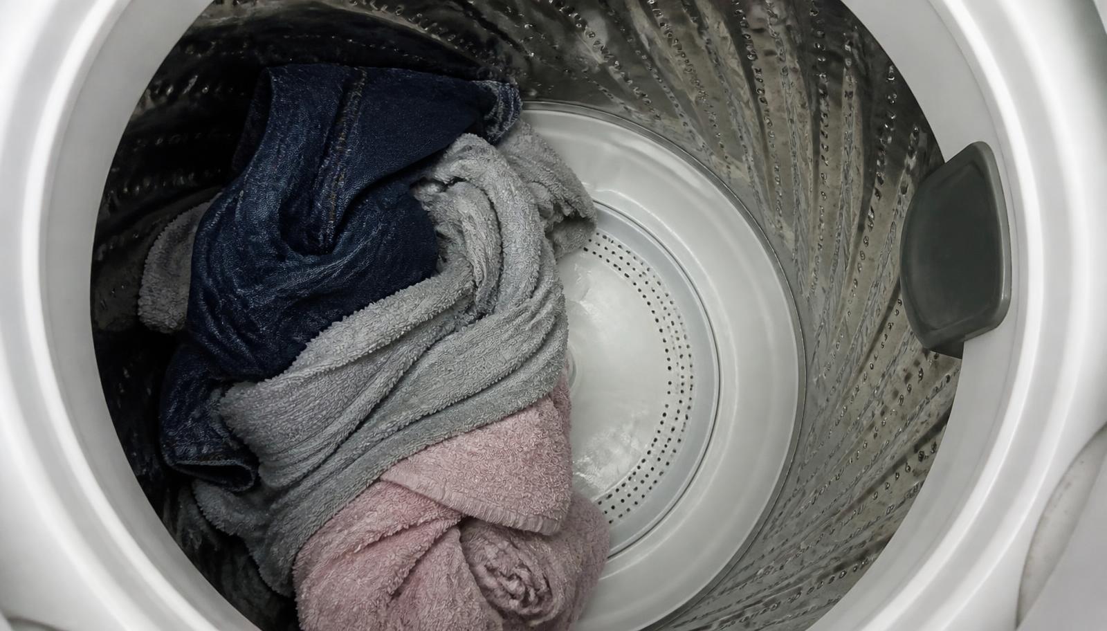 Roupas amontoadas de um lado só dentro do cesto de uma lavadora de abertura superior