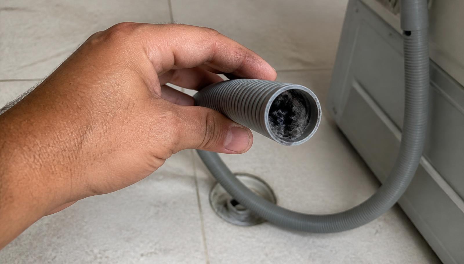Mão segurando a mangueira de saída de água de uma máquina de lavar em piso de lavanderia