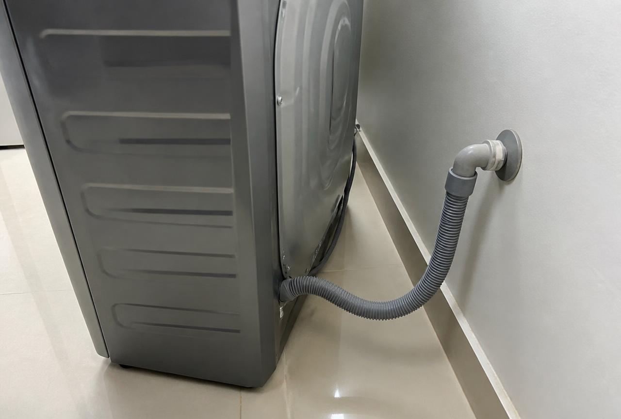 Mangueira de drenagem da máquina de lavar conectada ao ponto de esgoto na parede.