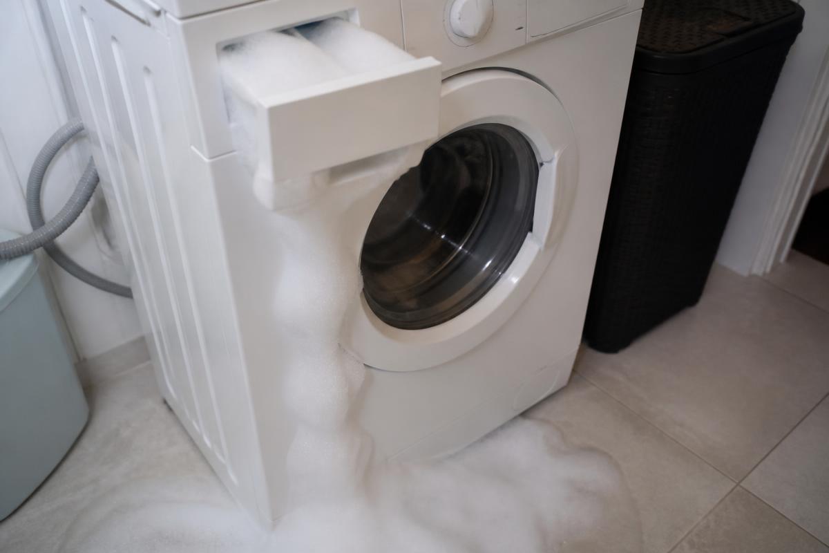 Espuma saindo pela gaveta de sabão de uma máquina de lavar e escorrendo pelo piso