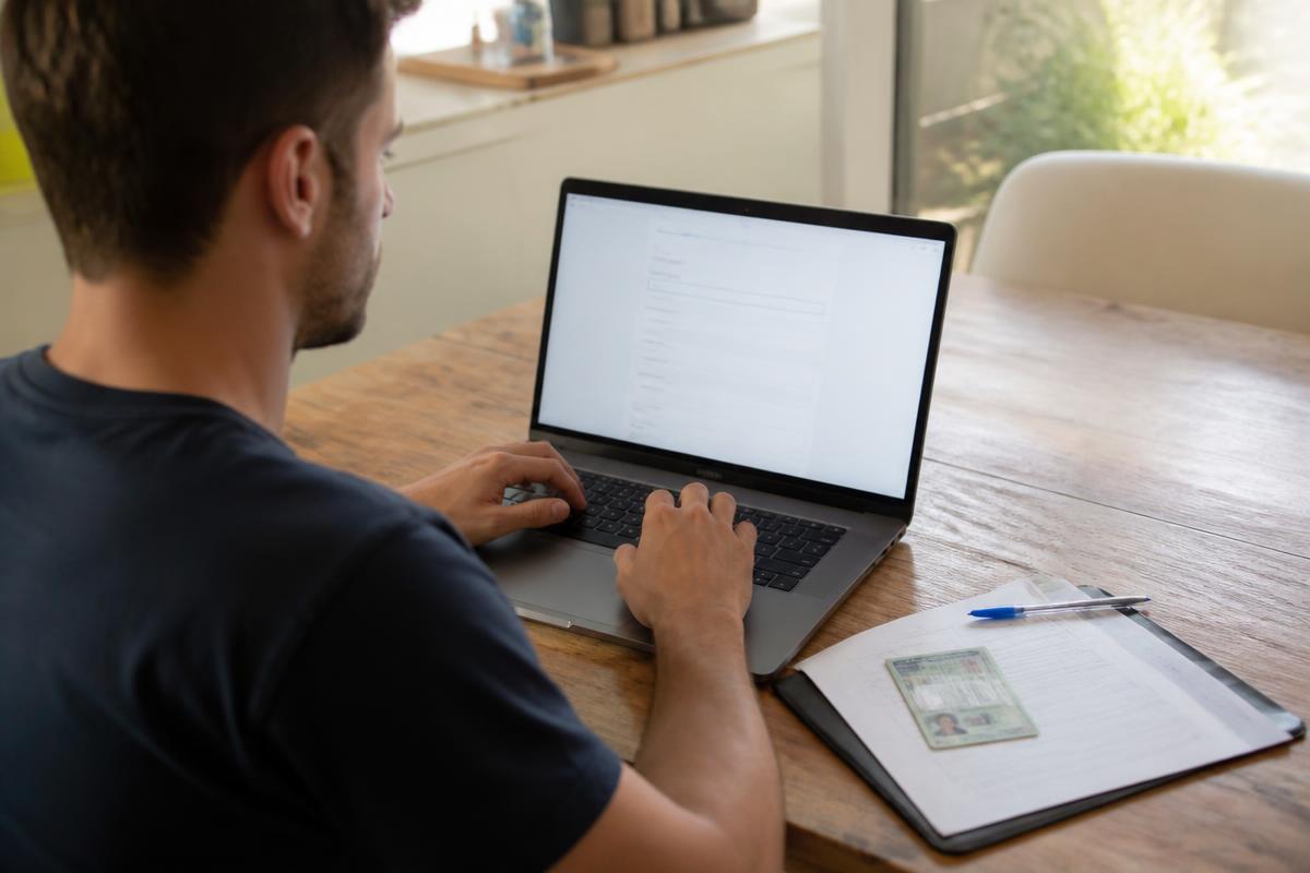 Homem preenchendo cadastro de abertura de empresa no notebook com documentos ao lado