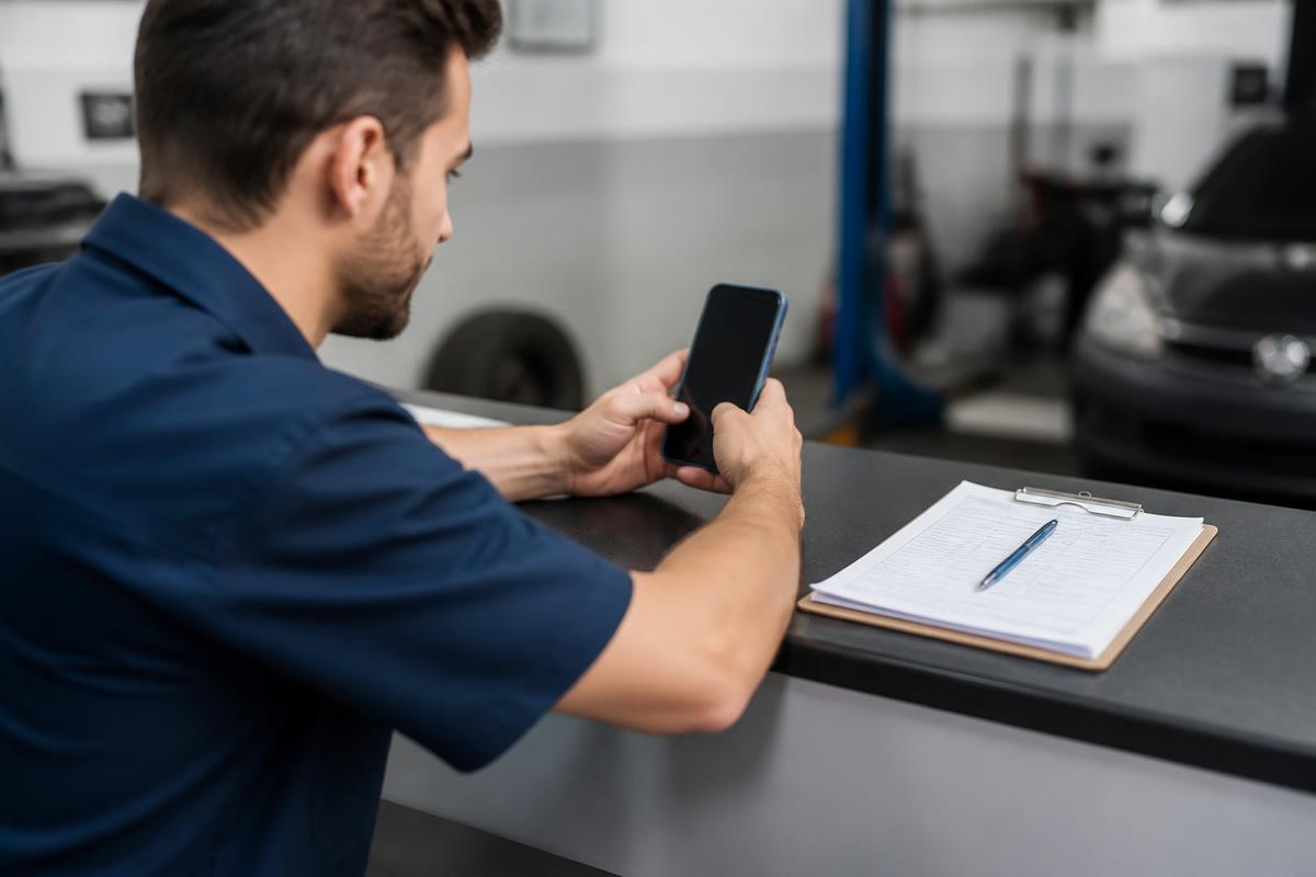 Técnico registrando atendimento pelo celular no balcão da oficina, com prancheta ao lado