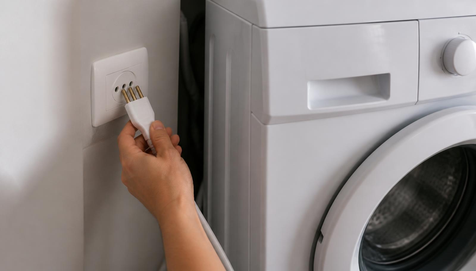 Mão puxando o plugue da tomada de parede atrás de uma lava e seca branca para fazer o reset