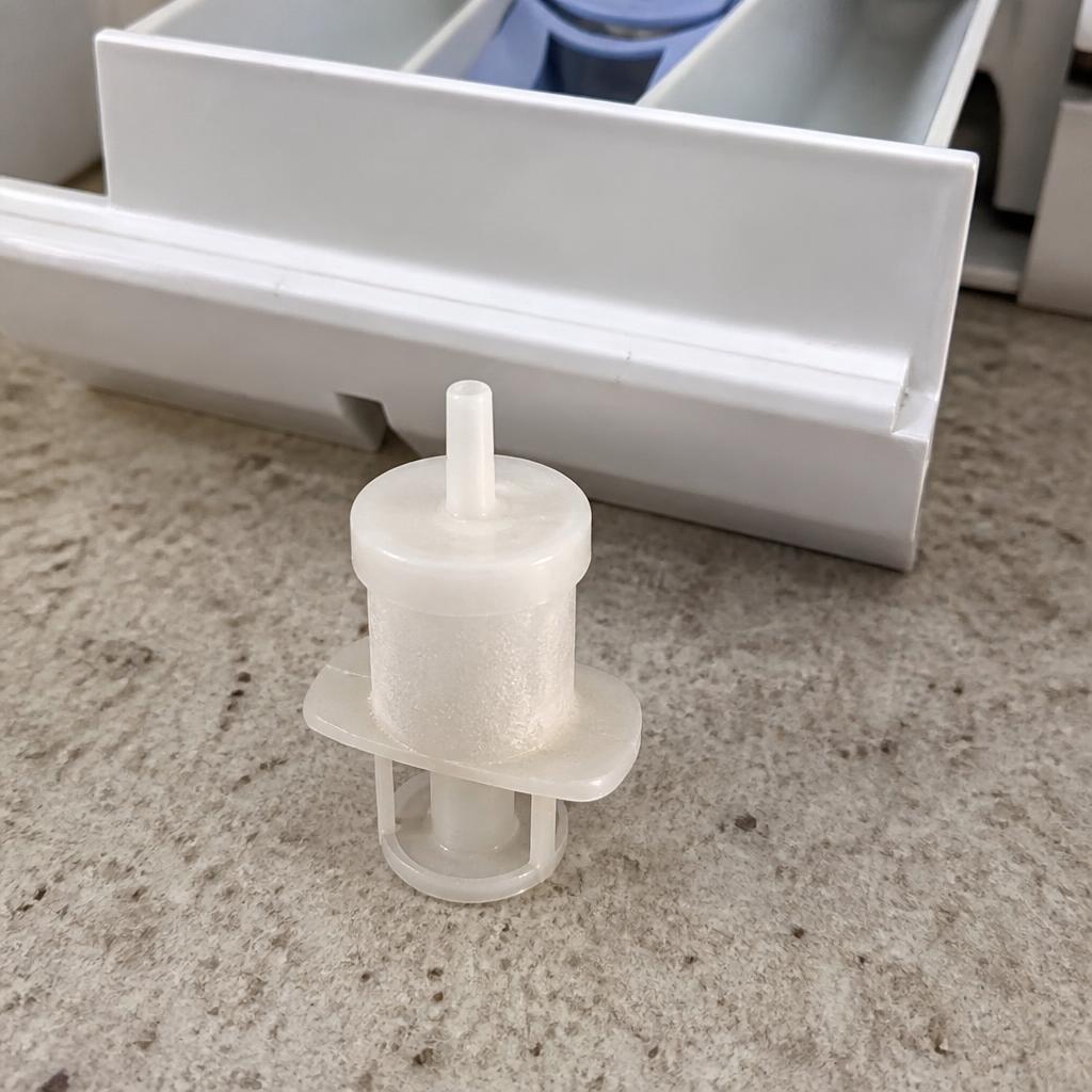 Sifão plástico do compartimento de amaciante retirado para limpeza sobre bancada ao lado da gaveta do dispenser