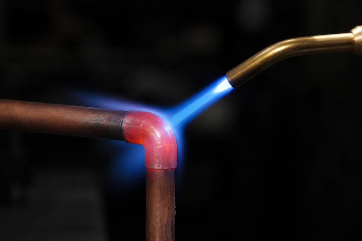 Chama azul de maçarico aquecendo junta de tubo de cobre até o vermelho cereja